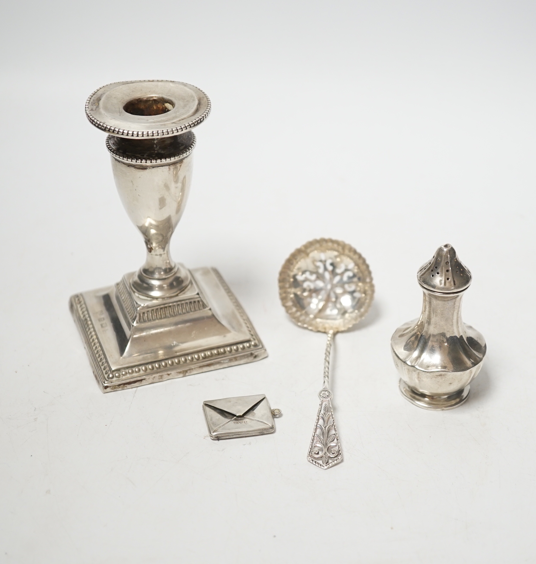 An Edwardian novelty silver 'envelope' stamp case, Albert Ernest Jenkins, Chester, 1905, 26mm, together with a silver mounted dwarf candlestick, a silver sifter spoon and a silver pepperette.